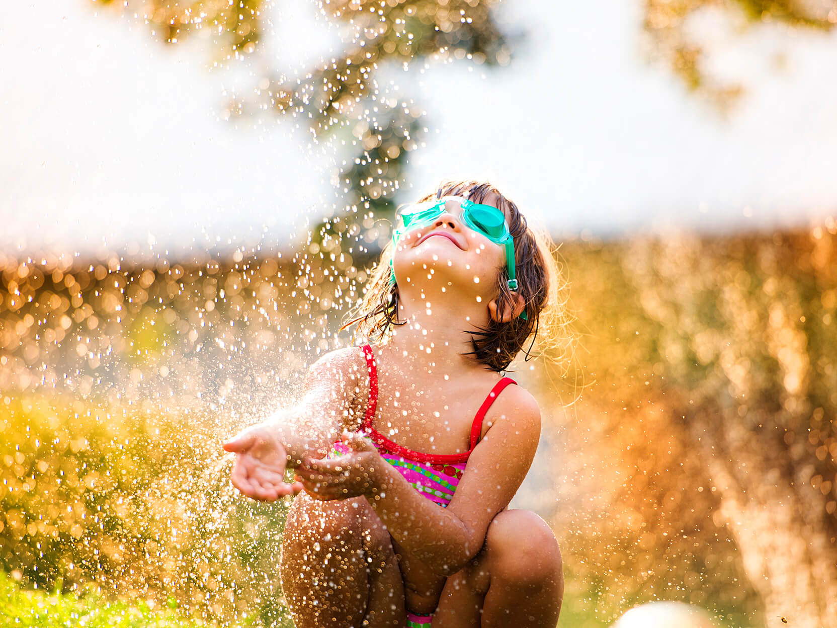 Child with goggles playing in sprinkler.