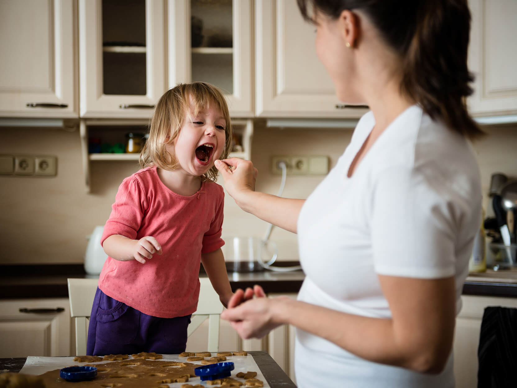 Woman feeding daughter cookies they are baking together.