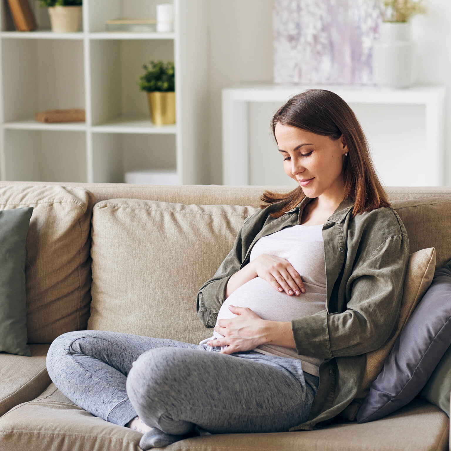 Pregnant woman sitting on couch holding her stomach.