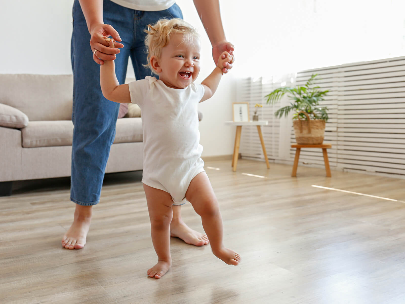 Baby walking with mother holding hands.