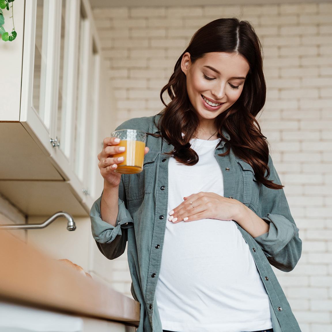 Woman holding a glass of juice with her hand on her pregnant belly.