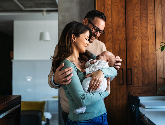 Man and woman holding their new baby, smiling.