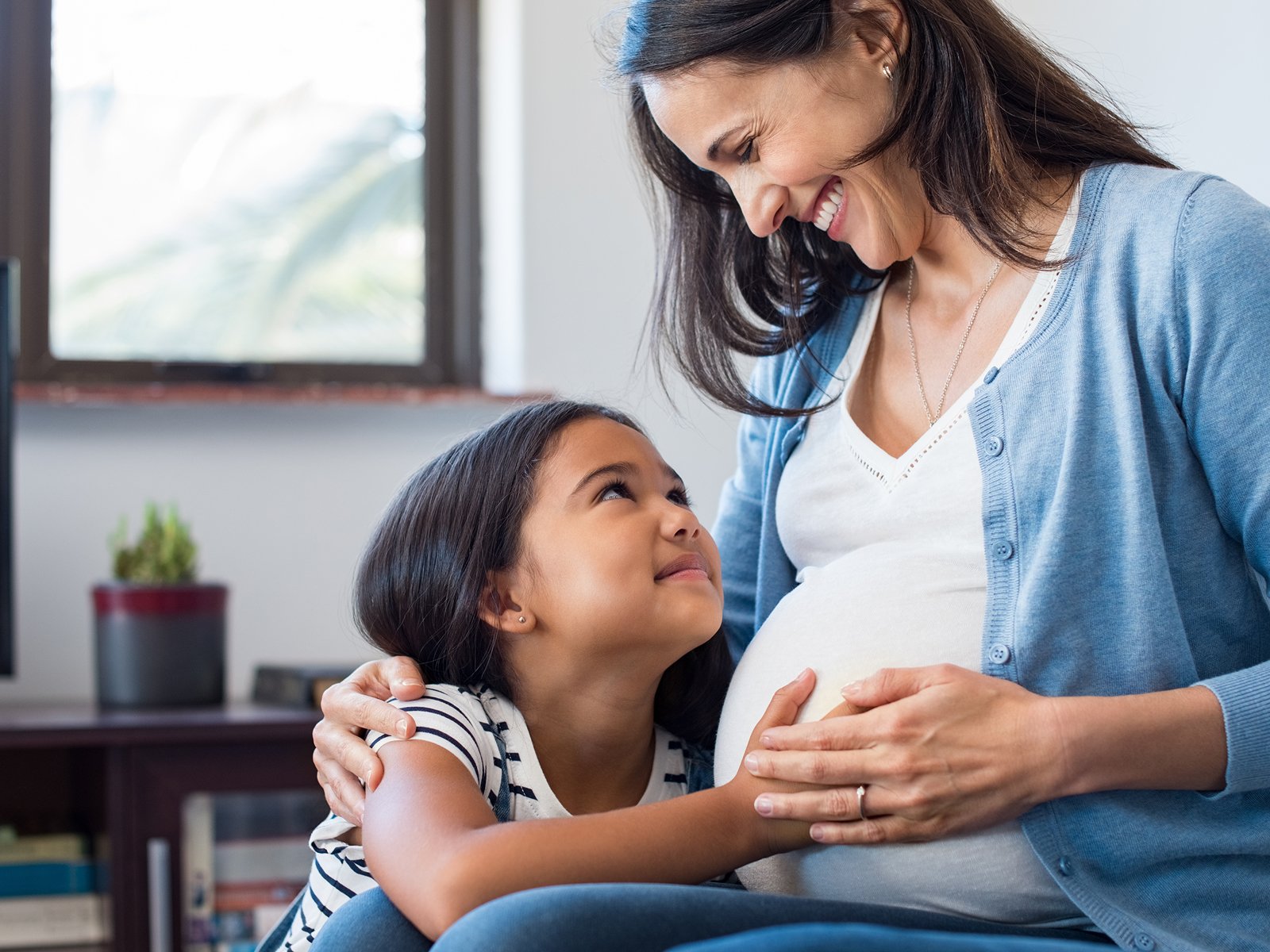 Child with her hand on pregnant mothers belly.